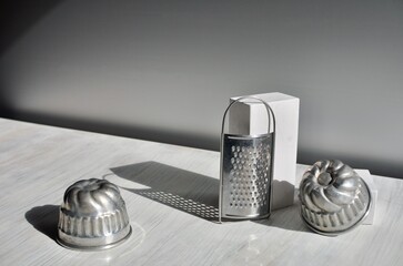 Two muffin tins and little grater on the white table against gray background.