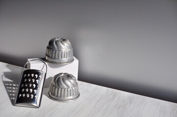 Two muffin tins and little grater on the white table against gray background.