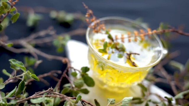High-Quality dolly shot of holy basil leaves along with its herbal tea in a glass cup beside it. Ocimum basilicum or Tulsi tea on a wooden surface, HD footage 24FPS.