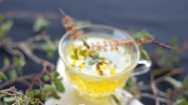 High-Quality dolly shot of holy basil leaves along with its herbal tea in a glass cup beside it. Ocimum basilicum or Tulsi tea on a wooden surface, HD footage 24FPS.