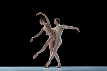 Impressive young man and woman, talented, professional dancers performing ballet art against black...
