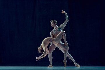 Muscular young man and beautiful woman, ballet dancers making artistic performance, dancing against blue studio background. Concept of beauty, classical dance style, inspiration, movements. Ad