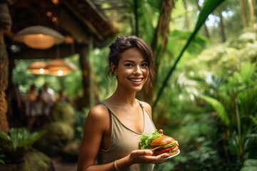 Medium shot portrait photography of a satisfied girl in her 30s holding a piece of hamburger against a lush tropical jungle background. With generative AI technology