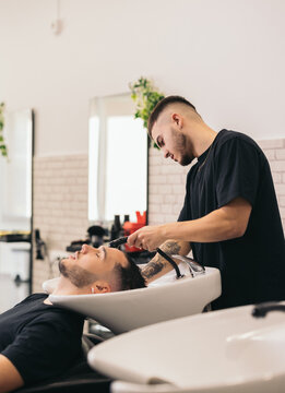 Young barber washing hair in barber shop