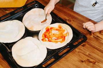 Close-up child smearing tomato sauce on tortillas dough, cooking homemade mini pizza