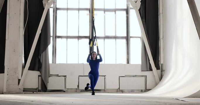 Fit young woman in athletic wear performing single leg squats with a leg extension, alternately raising one leg in front and sweeping it back while maintaining balance. Strengthening exercise.