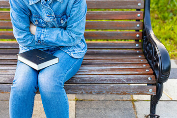 woman holding a bible sitting on a bench.