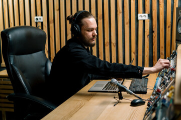 young sound engineer with headphones working in a music studio with monitors and an equalizer...