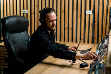young sound engineer with headphones working in a music studio with monitors and an equalizer...