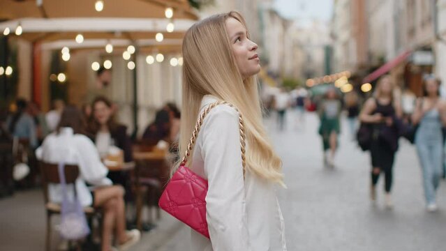 Portrait of blonde young woman tourist walking in urban city street background in summer daytime. Teenager girl traveler smiling having positive good mood enjoying outdoors. Town lifestyles, vacation