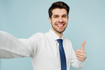 Close up young employee business man corporate lawyer wears classic formal shirt tie work in office doing selfie shot pov on mobile cell phone show thumb up isolated on plain blue background studio.