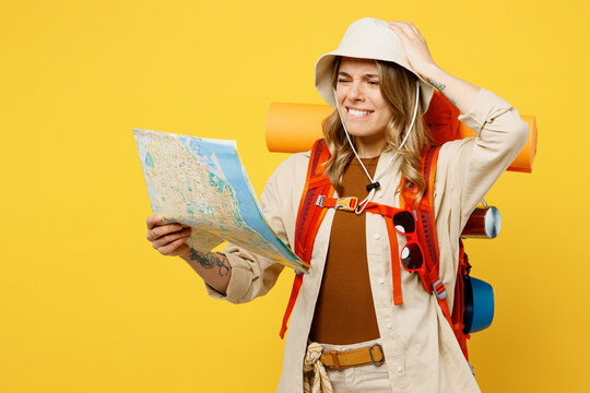 Young sad woman carry backpack with stuff mat hold map hold head say oops isolated on plain yellow background. Tourist leads active lifestyle walk on spare time. Hiking trek rest travel trip concept.
