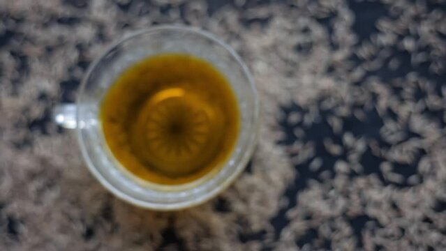 Hd footage 24 FPS. Cinematic close-up shot of cumin seeds or zeera aka jeera (Cuminum cyminum) in a glass bowl along with its herbal tea in a cup next to it on glossy surface, 
