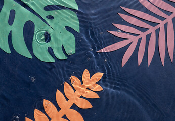 Dark blue water wavy surface background with colorful hand cut paper tropical leaves.	