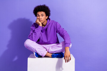 Full length photo of cool indifferent guy dressed violet hoodie siting on white platform arm on...