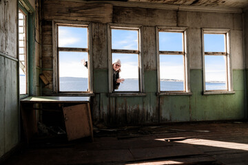 A cheerful woman looking into an empty window opening of an old wooden abandoned landing stage