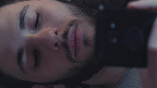 Vertical video. Mobile chat. Gadget leisure. Internet communication. Relaxed lazy man using phone reading texting message online at night.