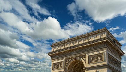Fototapeta na wymiar Arc de Triomphe (against the background of sky with clouds), Paris, France. The walls of the arch are engraved with the names of 128 battles and names of 660 French military leaders (in French)