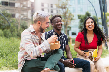 Young multiracial friends eating take-out street food in the city park during job meal break