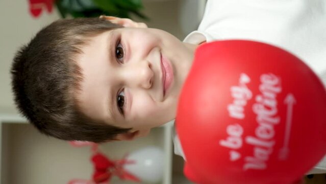 Cute 5 year old boy holds a balloon with the text be my valentine and smiles looking into the camera