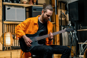 portrait of young rock artist with electric guitar in recording studio playing own track musical instrument drums on background
