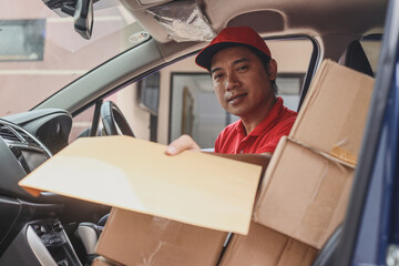 Delivery man smiling while sitting behind the wheel of a van and giving package, delivering mail.