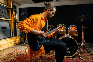 portrait of young rock artist with electric guitar in recording studio playing own track musical...