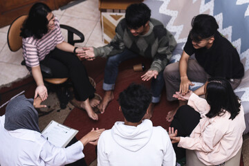 Overhead view of group therapy patients sitting in circle and holding hands during session to support each other 