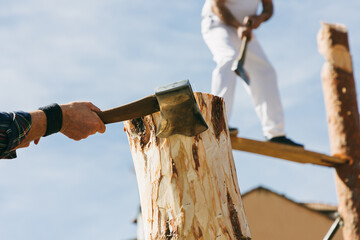 Men cut logs with axes at a city competition in honor of Woodcutter's Day.