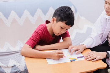 Child psychologist talking to boy while he drawing on white paper. Psychology, psychotherapy, professional counseling mental help for children