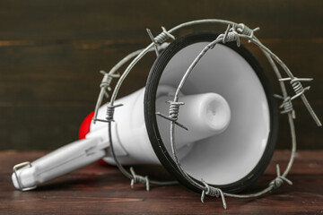 Megaphone with barbed wire on dark wooden background. Censorship concept