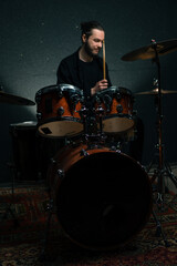a young male drummer plays a drum kit in a recording studio at a professional musician's rehearsal recording a song
