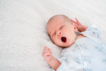 Little newborn baby boy lying on white bed and yawning