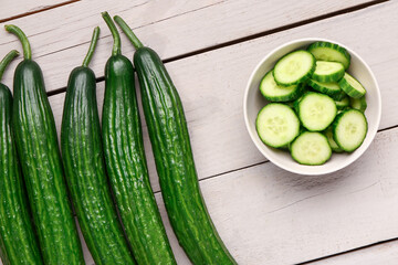Bowl with cut and whole cucumbers on light wooden background, closeup