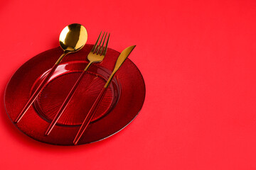 Table setting with clean plate and cutlery on red background