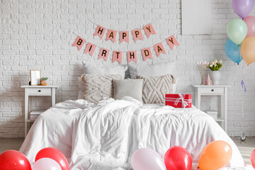 Interior of bedroom decorated for birthday with balloons, gift box and garland