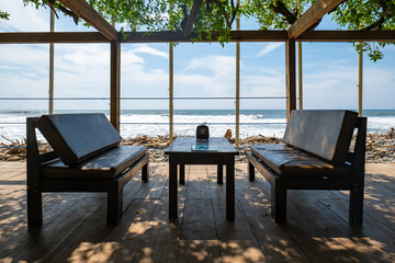 Sleek Set of Table and Chair on a Wooden Dock by the Pacific Ocean Under the Shadow of a Green Plant Roof