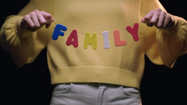Caucasian Woman Holding Up the Word "Family" in Colorful Letters, Slow Motion. Shot with ARRI Alexa in ArriRaw at 120 fps, exported 23.98 fps QuickTime Apple ProRes 422 HQ.