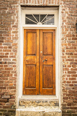 Double wooden doors on the front of a brick home with a window.