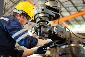 Professional caucasian white ethnicity male technician operating the heavy duty machine in the lathing factory. Technician in safety and helmet suit controlling a machine in factory.