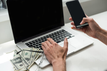 Mixed race man in glasses working with multiple electronic internet devices. Freelancer businessman has tablet and cellphone in hands and laptop on table with charts on screen. Multitasking theme