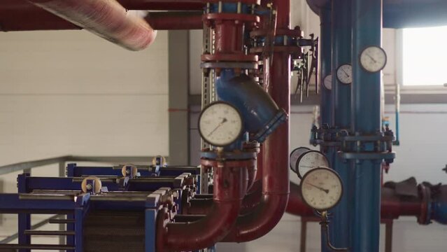 Metal pipes with manometers and powerful pumps in mechanical room. Heat generating system installed in modern building basement. Temperature adjustment
