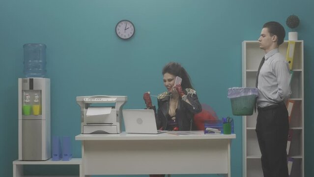 A woman sitting at her desk in the office speaks on a smartphone. An office worker holds a wastebasket into which a woman throws her phone, and starts typing on her laptop. HDR BT2020 HLG Material