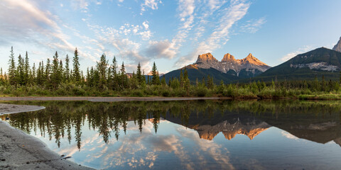 Panoramic view of the Three Sisters in Canmore, near Banff National Park in summer with sunset view over wilderness area panorama.