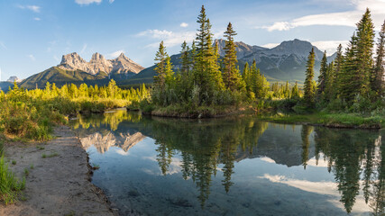 Mountain peaks reflecting in the calm water below at Three Sisters in Canmore, near Banff National...