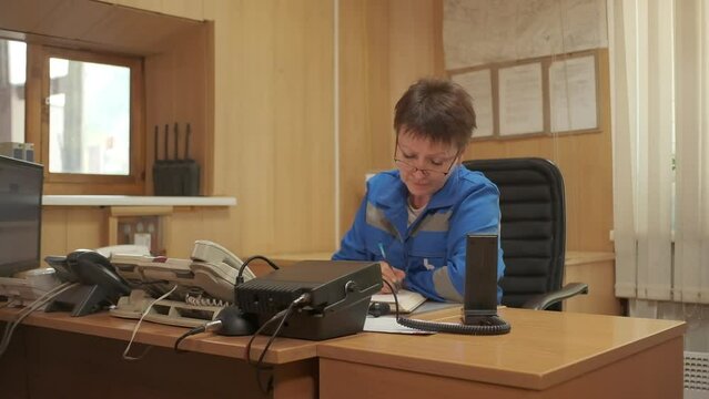 Woman in blue uniform working at the table. Clip. Emergency worker doing administrative work and writing.