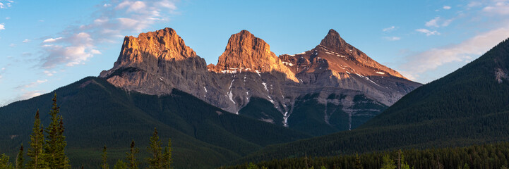 Obraz premium Golden sunset peaks near Banff National Park with Three Sisters at Canmore in view. Sun shining bright on the stunning panoramic view of wilderness, nature scenery in Canada.