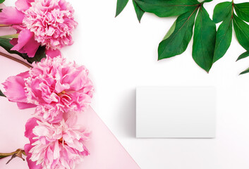 Obraz premium Composition of pink peonies, leaves, blank card on a white and pastel pink background. Fresh flowers. Floral content for Birthday, Valentines Day, Womens day. Flat lay, top view, close up, copy space