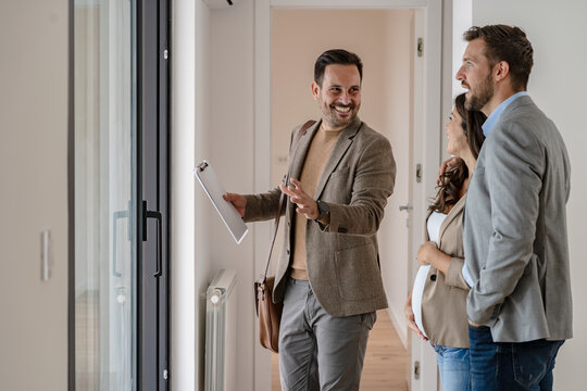 A young couple with a real-estate agent visiting an apartment for sale or for rent. Married couple buying an apartment. Real estate concept.
