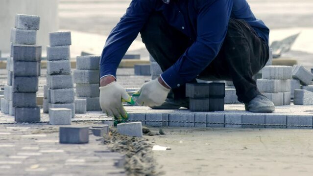 City worker compacts paving slabs with rubber hammer according leveling rope in city park crop body. Blocks of paving slabs prepared for work